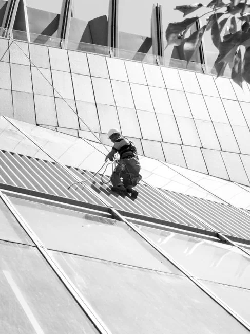services-03 Un homme méconnaissable portant des gants en latex jaunes nettoie un robinet doré dans une salle de bain, tout en faisant le ménage avec une éponge orange et du détergent