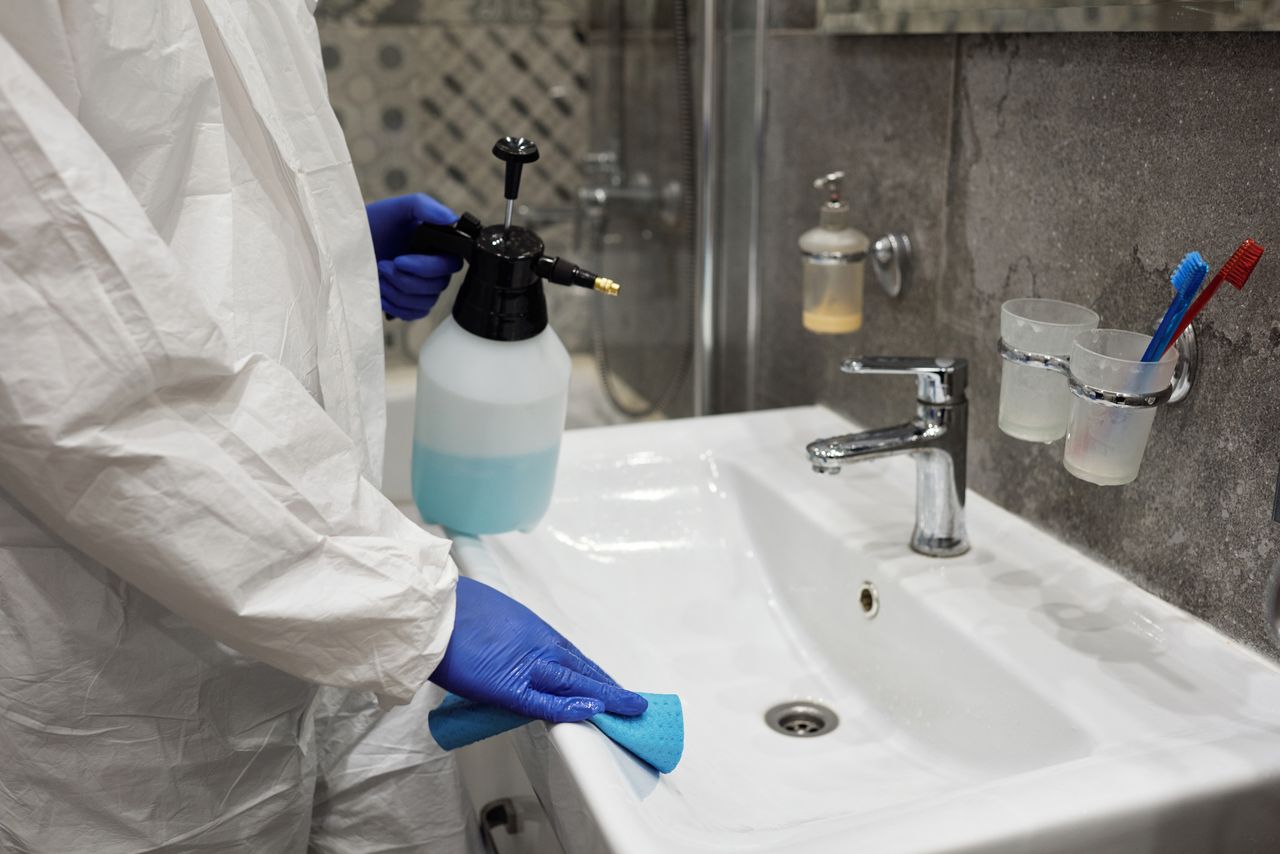 services-02 A person sanitizing a bathroom sink with a spray bottle, ensuring hygiene.