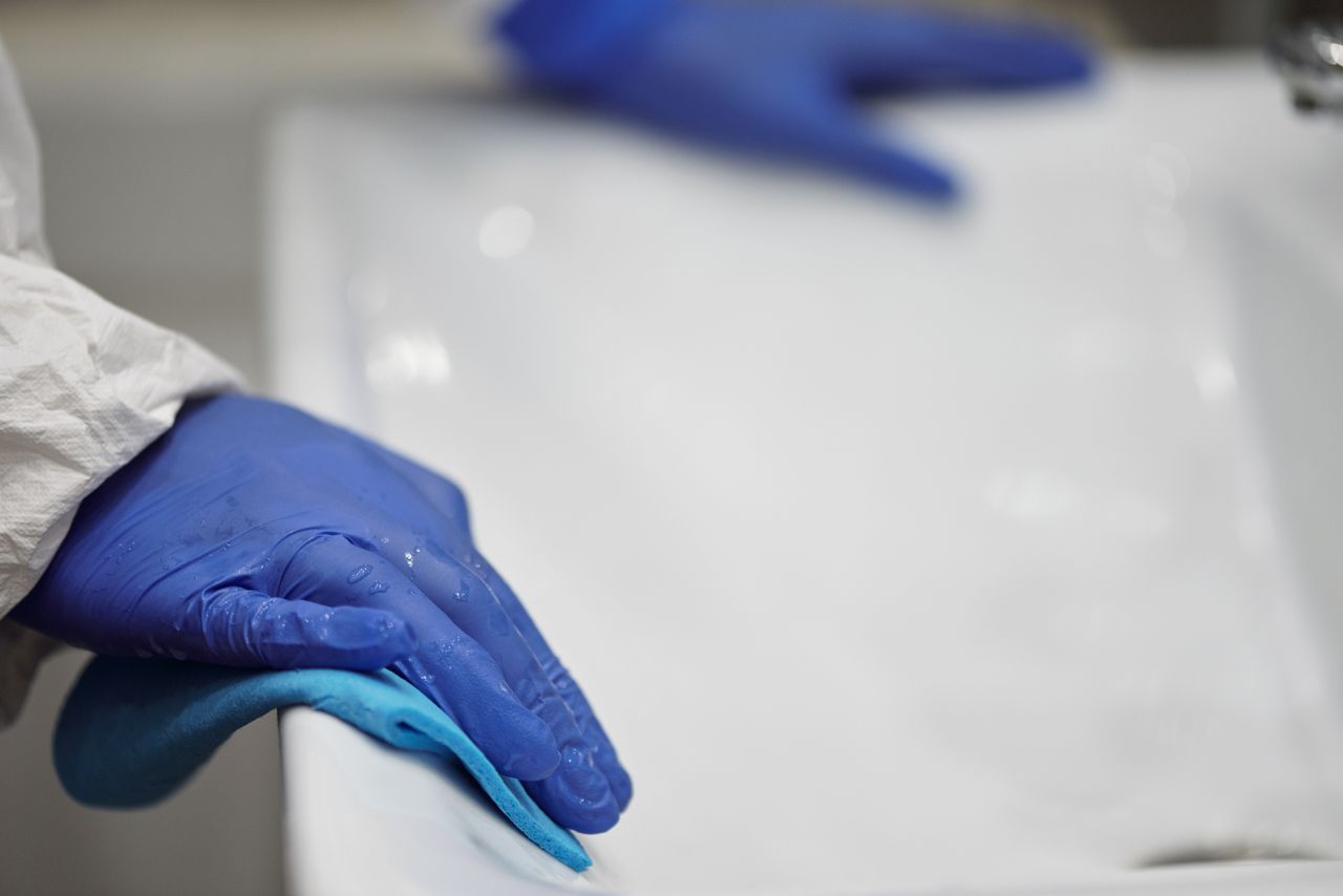 services-03 Close-up of a person sanitizing a bathroom sink with gloves and cloth, focusing on hygiene and cleanliness.